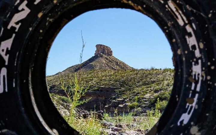 a mesa dotted in green desert shrubs is shown through a tire